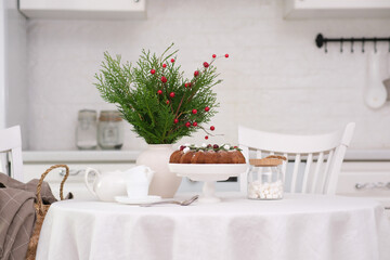 Christmas home interior in white kitchen-Christmas chocolate bundt cake with fresh berries and rosemary. Winter baking at Christmas. Ceramic vase with spruces brunches..