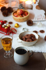 Cup of tea or coffee, glass of wine or juice, bowl of cookies, organic pomegranate, fluffy blanket, pine cones, various Christmas decorations and lit candles on the table. Christmas hygge concept.