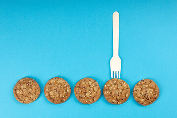 a row of five round oatmeal cookies are laid out in a row, a fork over one cookie