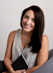 Fototapeta premium business woman against a white wall holding a notebook sitting on a chair 