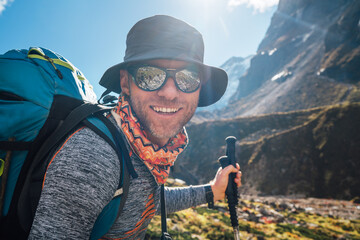 Portrait Young hiker backpacker man in sunglasses smiling at camera in Makalu Barun Park route during high altitude acclimatization walk. Mera peak trekking route, Nepal. Active vacation concept image - obrazy, fototapety, plakaty