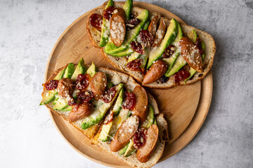 Avocado sourdough bread toast with sausage and sun-dried tomato on wooden plate. Healthy food...