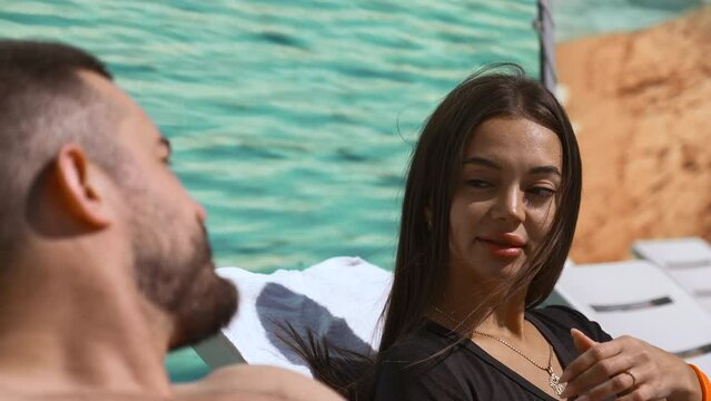 Couple sunbathing near pool. Clip. Beautiful man and woman lying on sunbeds outdoors under the shining sun.