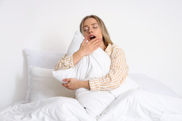 Young woman with pillow yawning in bedroom