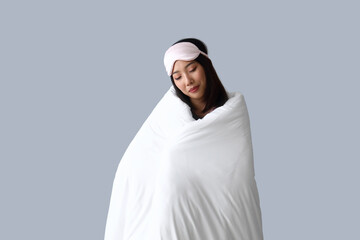 Beautiful Asian woman with sleeping mask and blanket on grey background