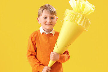 Happy little boy with school cone on yellow background