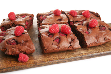 Wooden board with pieces of raspberry chocolate brownie on white background