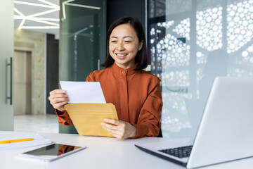 Successful satisfied business woman received mail envelope letter with good news message, Asian woman at workplace reading document paper, smiling at workplace inside office.