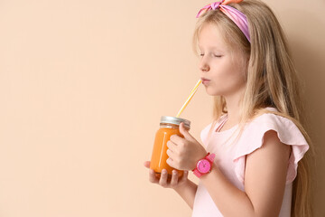 Little girl with glass jar of juice on beige background