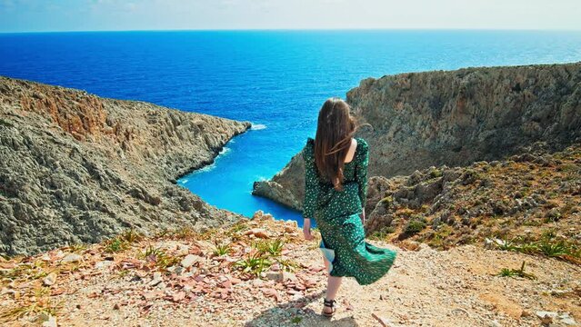 A beautiful girl looking at the sandy beach in a cove surrounded by rock formations at Seitan Limania, Crete. A young woman enjoying the picturesque panoramic views with a stunning crystal blue beach.