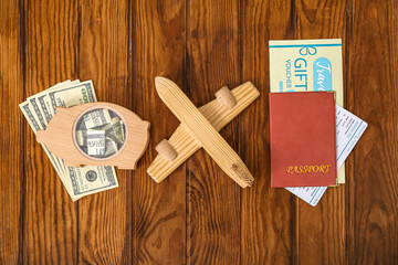 Piggy bank with money, toy airplane and travel gift voucher on brown wooden background. Concept of savings for travel