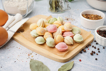 Wooden board with colorful raw dumplings and different spices on white background