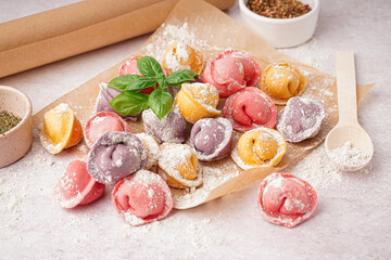 Baking paper with colorful raw dumplings and basil on white background