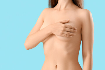 Fototapeta premium Naked young woman covering her breast on blue background