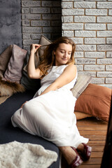 A young woman in a long white dress lies on the floor on pillows and relaxes