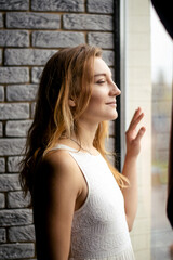 Fototapeta premium A young lady, dressed in ethereal white, beams near the vast window, her joy mirroring the morning sun. Embodying hope and happiness, she welcomes the new day with open arms