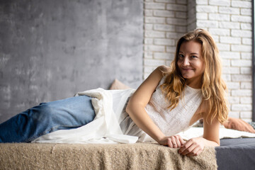 Relaxing on the sofa, the young woman wears jeans and a white top, embracing tranquility in her leisure time