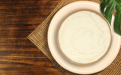 Cup of curd in a plate on wooden table with a burlap underneath. Copy space table top view.