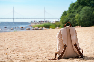 The backpack stands on the sand against the background of the bridge in Saint Petersburg