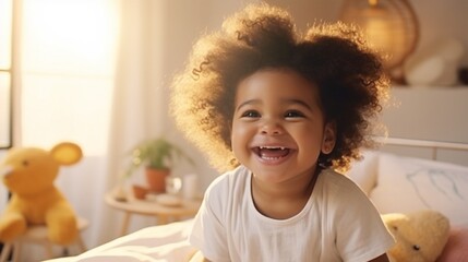 Smiling black baby with afro hair sitting on bed and smiling to camera.