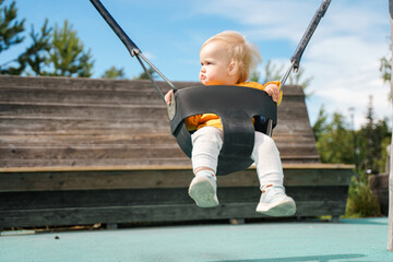 Cute little child baby on a swing in summer in the park