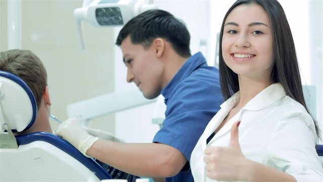 The dentist examines the teeth and smiles at him and the girl-assistant teeth smile directly at the camera and thumb up
