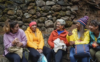 Multiracial women with different ages resting and having fun together during trekking day in the forest - Multi generational female friends - Focus on african woman face