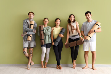 Group of sporty young people with yoga mats near green wall