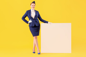 Young stewardess with blank poster on yellow background