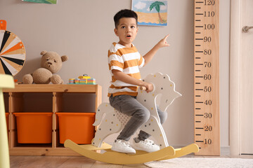 Little Asian boy rocking on horse at home