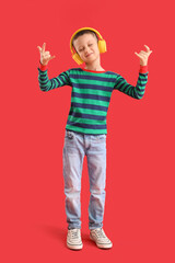 Cute little boy in headphones showing "devil horns" on red background