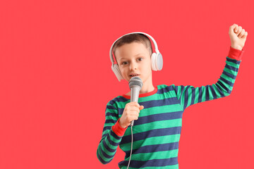 Cute little boy in headphones with microphone singing on red background