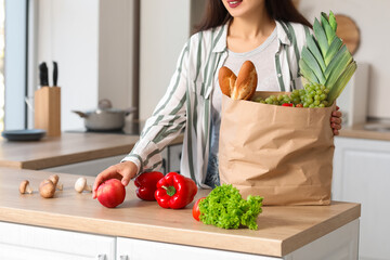 Young Asian woman unpacking fresh products from market at table in kitchen