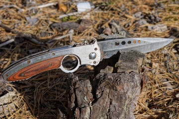 one large hunting folding knife sticks out in the brown bark of a pine stump in nature in the forest