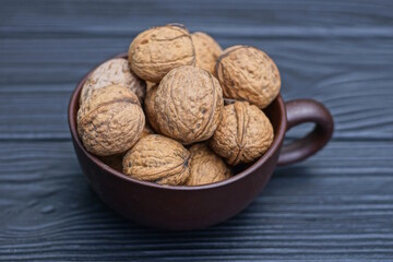 a bunch of walnuts in a brown ceramic cup stands on a black wooden table