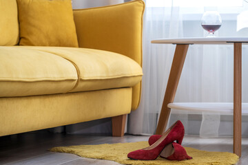 red women's high-heeled shoes lie on the floor in the room near the yellow sofa and table