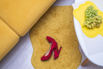 red women's high-heeled shoes lie on the floor in the room near the yellow sofa and table, top view