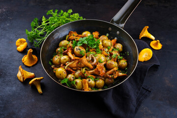 Traditional fried chanterelle with mini potatoes served as close-up in a rustic frying pan with...