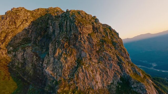 Mountain summit geology formation rock texture natural sunrise morning sunlight valley landscape aerial view. FPV sport drone shot extreme altitude cliff panorama snow green grass ecology environment
