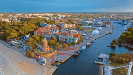 This aerial shot focuses on Kołobrzeg's iconic lighthouse and the thriving harbor beneath it. The coastal charm, combined with the maritime atmosphere of this Polish gem, is beautifully showcased. - obrazy, fototapety, plakaty