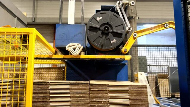 Ready-made cardboard boxes are moved in stacks along an automated packaging line. The strapping machine packs the stacks with thick white thread. Paper corrugated box factory.