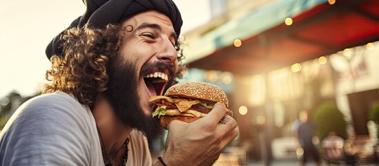 Young man eating burger outdoors close up Street food being enjoyed by bearded man - obrazy, fototapety, plakaty