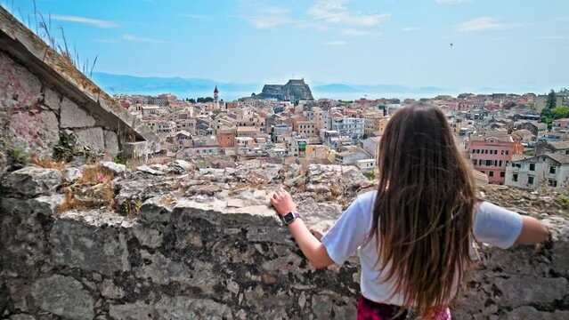Beautiful woman enjoying the view of the traditional Greek cobblestone streets and pastel-coloured Venetian architecture. Girl looking from above of the Kerkyra city from New Venetian Fortress.