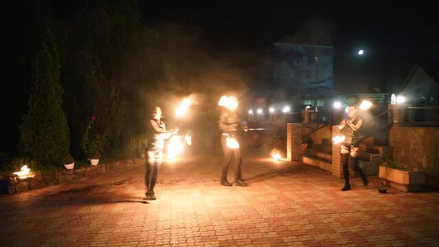 Fire performance show. Artists spin burning poles at night. Outdoor tribal dance with flames. Man and women dancers troupe act with torches at venue for tourists. Fire arts team juggling on festival.
