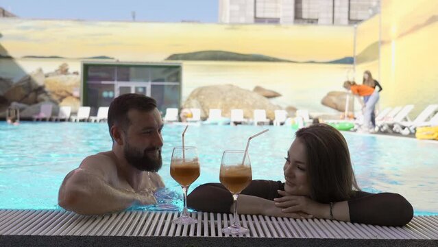 Young Muscular Man Trying To Pick Up A Brunette Girl In A Swimming Pool. Clip. Man Flirting With A Woman, Couple Enjoying Cocktails.