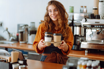 A beautiful coffee shop owner holds paper cups with hot takeaway drinks in her hand. Young female...