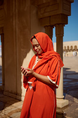Young Arabic Muslim woman praying, making Islamic pray dua with cupped hands standing near marble columns at mosque