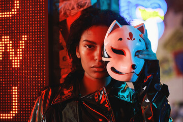 Young African American woman putting on or taking off fox mask and looking at camera while standing...