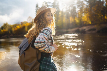Beautiful woman traveler enjoying autumn hiking along the river. A traveler walks in the autumn...