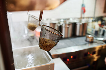 Focus on one of two metallic colanders with boiled ramen hanging over metallic sink in spacious...